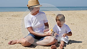 Mom and son are sitting on the beach on a sunny summer day. Family vacation and picnic in nature. The child eats and