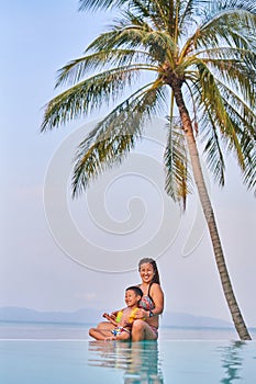 Mom and son are sitting on the edge of the pool in the lotus position