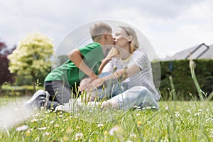 mom and son are sitting on the green grass in the park and kissing