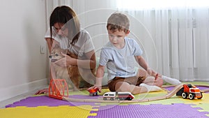 Mom and son spend time together playing a toy railroad in nursery on puzzle mats