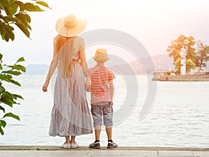 Mom and son standing on the pier on the sea background, lighthouse and mountains in the distance. Back view