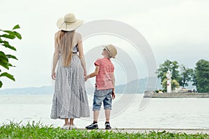 Mom and son standing on the pier. Sea on a background, lighthouse and mountains in the distance. Back view