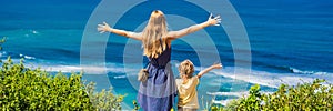 Mom and son travelers on a cliff above the beach. Empty paradise beach, blue sea waves in Bali island, Indonesia