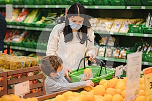 Mom and son wearing protective masks choose fruits to buy in the store.
