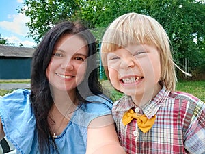 Mom and son with yellow bow tie smile and take selfies in the yard in the fresh air in outdoor. Young mother with her
