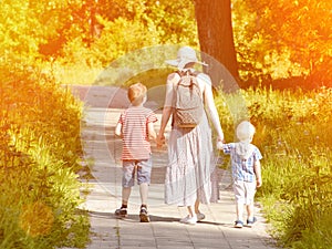 Mom and sons walking along the road in the park. Back view. Sunny day