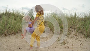 Mom spin her blond daughter around herself. Active family girls have fun in dune