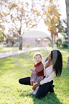 Mom squatted down next to a little smiling girl in a sunny meadow