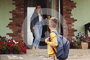 Mom, standing at the door near her house, escorts her son to school, back to school.