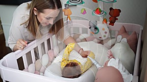 mom stands at crib of a newborn baby. furniture and toys for children's room.