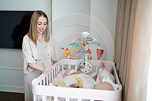 mom stands at crib of a newborn baby. furniture and toys for children& x27;s room.