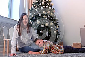 Mom stroking son on back near Christmas tree at home in living room, New Year.