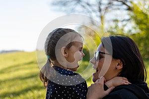 Mom in sunglasses and her little daughter have fun in the meadow at sunset