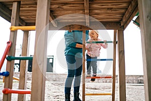 Mom supports a little girl climbing the stairs to the slide. Cropped