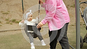 Mom swinging her little happy girl on the swing in the park, baby child on the playground