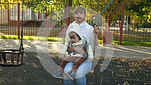Mom is swinging a small child on a swing in a proud park. Happy family. Mom and daughter go out on weekends. Family