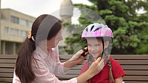 Mom takes care of her daughter's safety during outdoor activities, putting on her protective helmet.