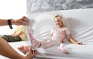 Mom takes off her little daughter`s socks and tickles her feet a little. The girl laughs