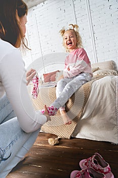 Mom takes off her little daughter`s socks and tickles her feet a little. The girl laughs.