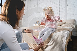 Mom takes off her little daughter`s socks and tickles her feet a little. The girl laughs.