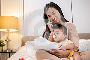 A mom is talking on the phone and working on documents while taking care of her little son