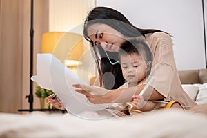 A mom is talking on the phone and working on documents while taking care of her little son