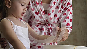 Mom teaches a child to cook dough. Mother and daughter stir with a whisk a mass of flour. Cooking at home with family