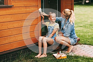 Mom teaches daughter to paint a house on the street with a brush. A happy family. Home Improvement, DIY Repair