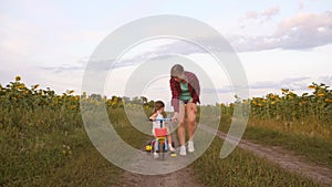 Mom teaches daughter to ride a bike on a country road in a field of sunflowers. A small child learns to ride a bike