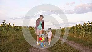 Mom teaches daughter to ride a bike on a country road in a field of sunflowers. a small child learns to ride a bike