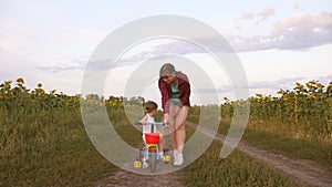 Mom teaches daughter to ride a bike on a country road in a field of sunflowers. a small child learns to ride a bike