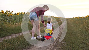 Mom teaches daughter to ride a bike on a country road in a field of sunflowers. a small child learns to ride a bike