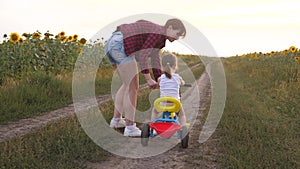 Mom teaches daughter to ride a bike on a country road in a field of sunflowers. a small child learns to ride a bike