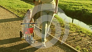 Mom teaches daughter to ride a bike in the park. Mother plays with her little daughter. The concept of a happy childhood