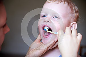 Mom teaches and helps her three-year-old son to brush his teeth