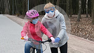 Mom teaches her daughter to ride a bike in the city Park. they are wearing protective helmets and medical masks. The concept of