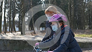 Mom teaches her daughter to ride a bike in the city Park. they are wearing protective helmets and medical masks. The concept of