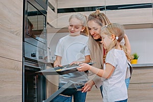 Mom teaches her daughters to cook in the kitchen. The family bakes cookies in the oven