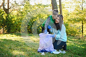 Mom teaches her son to clean up trash in nature. A woman removes plastic bottles in a bag. The topic of environmental pollution by