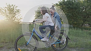 Mom teaches kid daughter to ride a bike, girl rides bicycle on country road, sunset natural landscape background.