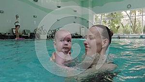 Mom teaches a little child to swim underwater in water baby class in the pool