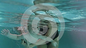 Mom teaches a little child to swim underwater in water baby class in the pool