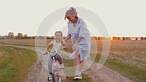 Mom teaches little daughter to ride bike at sunset outdoors nature