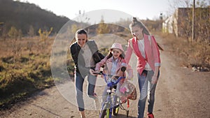 Mom teaches little girl to ride a bike on a warm autumn evening. The concept of a happy family.