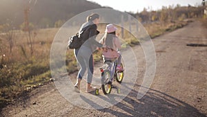 Mom teaches little girl to ride a bike on a warm autumn evening. The concept of a happy family.