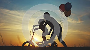 mom teaches son to ride a bike. happy family kid dream concept. mom and child son learn to ride a bike silhouette in the