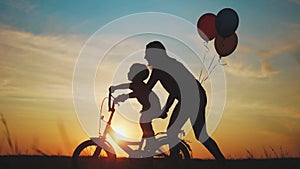 mom teaches son to ride a bike. happy family kid dream concept. mom and child son learn to ride a bike silhouette in the
