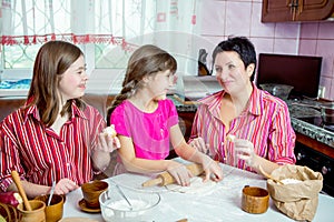 Mom teaching her two daughters cooking on the kitchen.