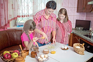 Mom teaching her two daughters cooking on the kitchen.