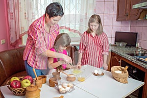 Mom teaching her two daughters cooking on the kitchen.